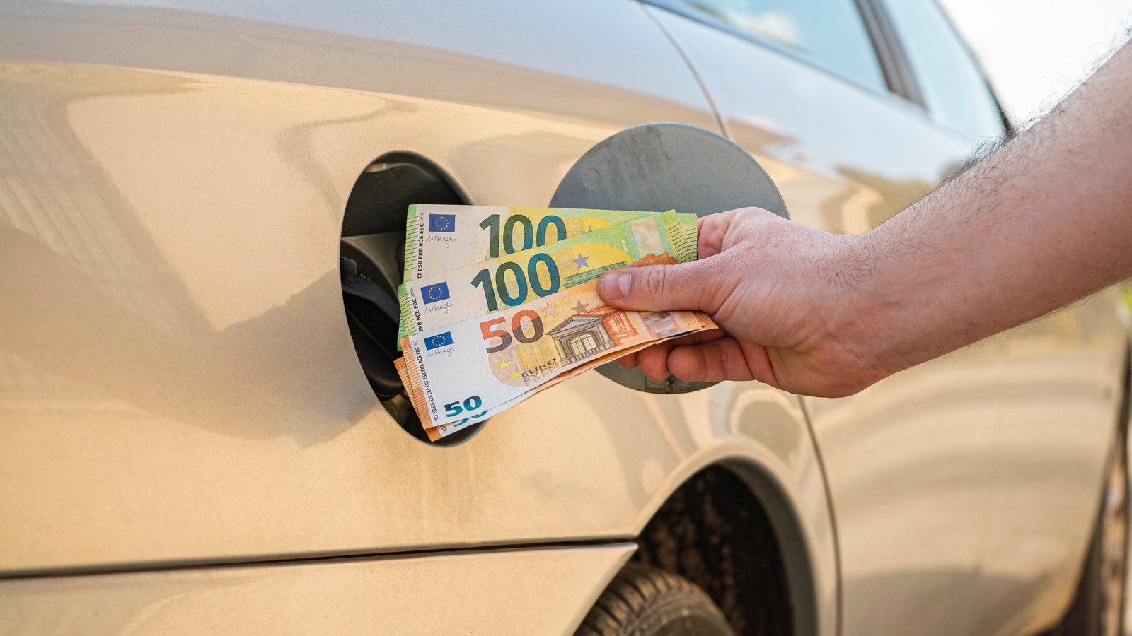 Hand die eurobiljetten in de tankopening van een auto steekt